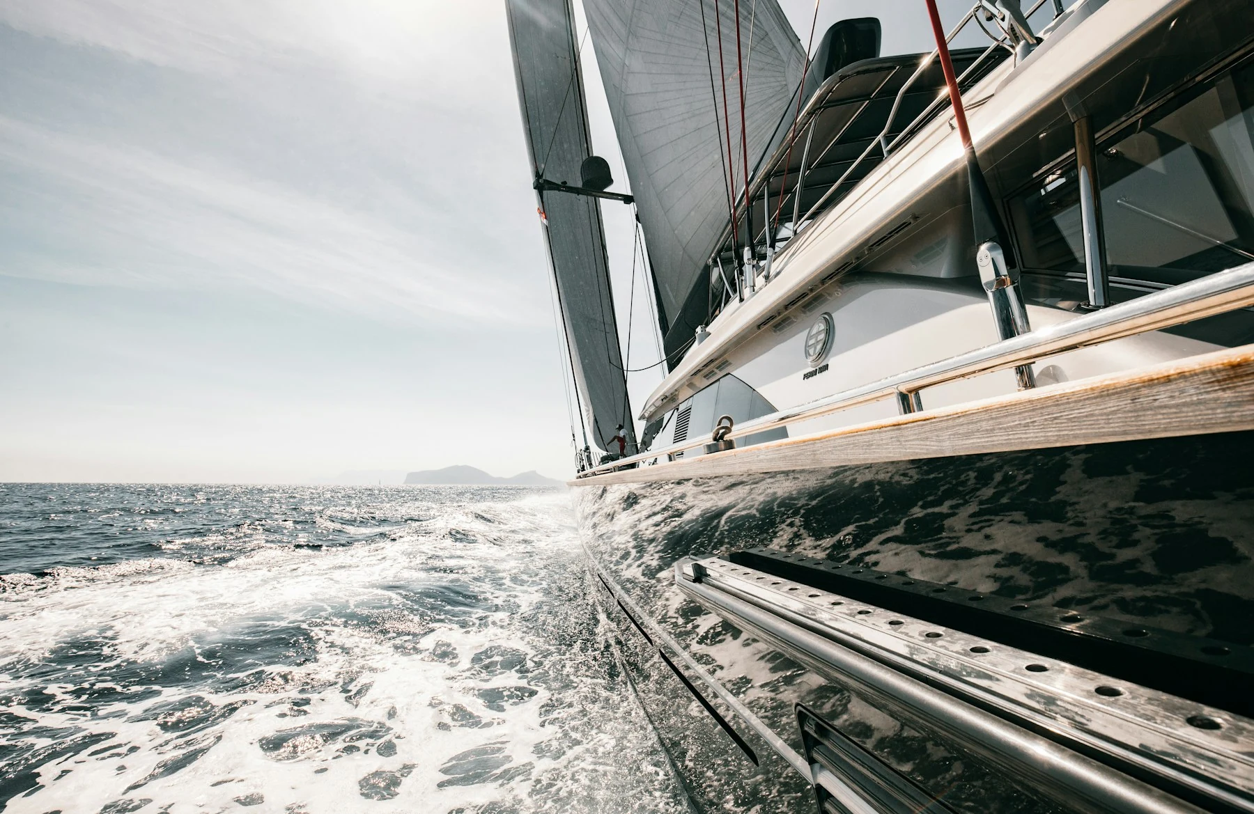 Yacht de luxe en navigation, coque sombre et sillage vus au ras de l’eau